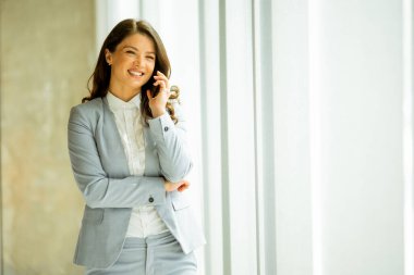 Ofis penceresinin yanında cep telefonu olan güzel bir kadın.