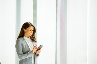 Ofis penceresinin yanında cep telefonu olan güzel bir kadın.