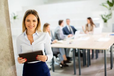 Ofis koridorunda dijital tabletle duran genç bir iş kadını.
