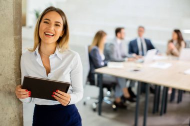 Ofis koridorunda dijital tabletle duran genç bir iş kadını.