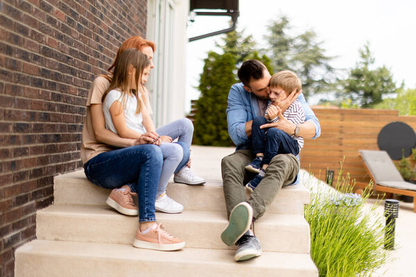 Family with a mother, father son and daughter sitting outside on  steps of a front porch of a brick house