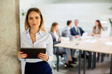 Ofis koridorunda dijital tabletle duran genç bir iş kadını.