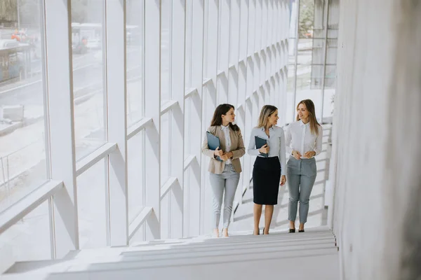 Three cute young business women walking on stairs in the office hallway
