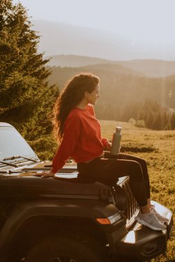 Pretty young woman relaxing on a terrain vehicle hood at countryside