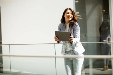 Ofis koridorunda dijital tablet üzerinde çalışan güzel genç bir kadın.