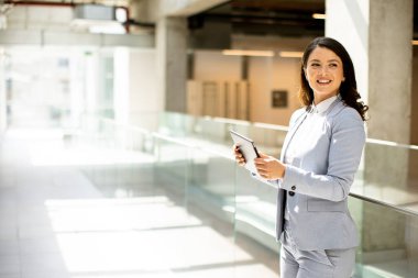 Ofis koridorunda dijital tablet üzerinde çalışan güzel genç bir kadın.