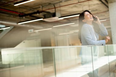 Ofis koridorunda cep telefonu kullanan genç ve güzel bir iş kadını.
