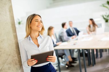 Ofis koridorunda dijital tabletle duran genç bir iş kadını.