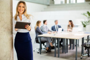Ofis koridorunda dijital tabletle duran genç bir iş kadını.