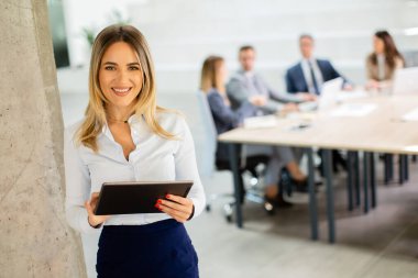 Ofis koridorunda dijital tabletle duran genç bir iş kadını.