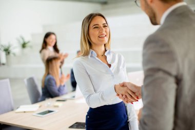 Ofiste iş arkadaşıyla tokalaşan genç ve güzel bir iş kadını.