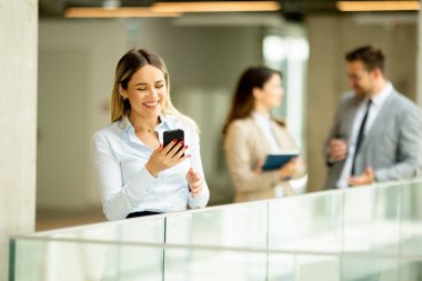 Ofis koridorunda cep telefonuyla duran genç bir iş kadını.