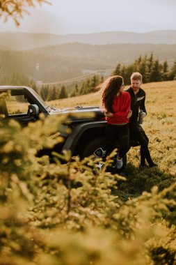 Handsome young couple relaxing by a terrain vehicle hood at countryside