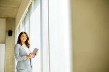 Ofis penceresinin yanında dijital tablet üzerinde çalışan güzel genç bir kadın.