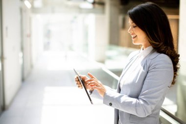 Ofis koridorunda dijital tablet üzerinde çalışan güzel genç bir kadın.