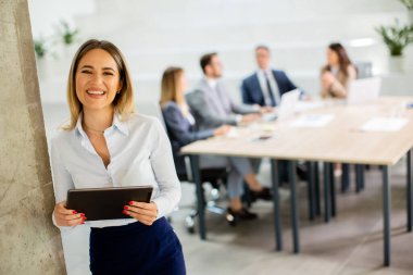 Ofis koridorunda dijital tabletle duran genç bir iş kadını.