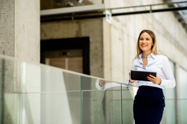 Ofis koridorunda dijital tablet üzerinde çalışan güzel genç bir kadın.