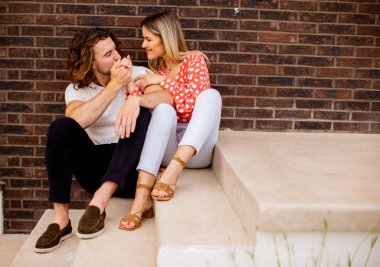 Tuğla duvarın önünde oturan güzel, gülümseyen, aşık genç bir çift.