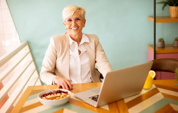 Mulher Sênior Usando Telefone Celular Enquanto Trabalhava Laptop Tomando Café — Fotografia de Stock