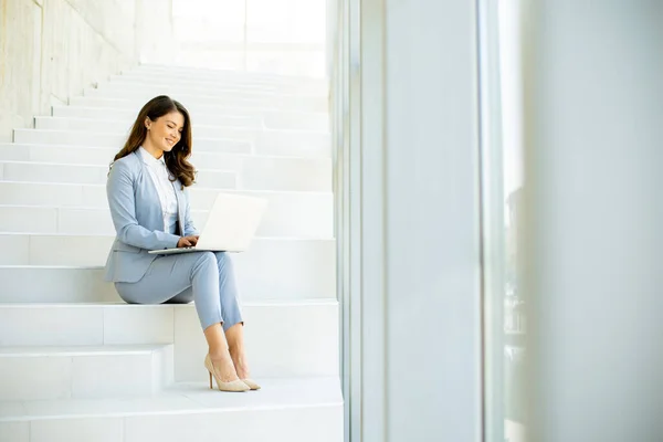 漂亮的年轻女商人坐在办公室走廊的楼梯上 在笔记本电脑上工作 — 图库照片