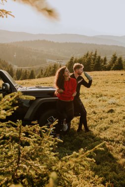 Handsome young couple relaxing by a terrain vehicle hood at countryside