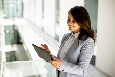 Ofis koridorunda dijital tablet üzerinde çalışan güzel genç bir kadın.