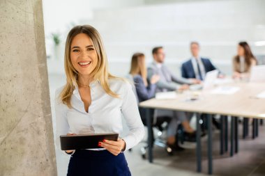 Ofis koridorunda dijital tabletle duran genç bir iş kadını.