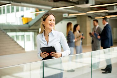 Ofis koridorunda dijital tabletle duran genç bir iş kadını.