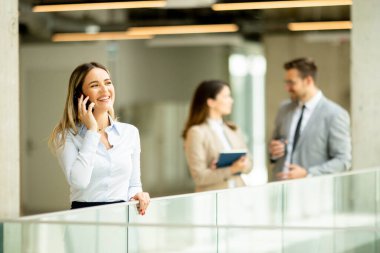 Ofis koridorunda cep telefonuyla duran genç bir iş kadını.