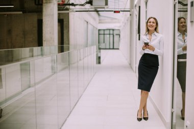 Ofis koridorunda cep telefonu kullanan genç ve güzel bir iş kadını.