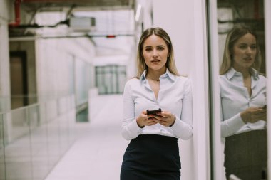 Ofis koridorunda cep telefonu kullanan genç ve güzel bir iş kadını.