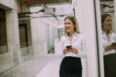 Ofis koridorunda cep telefonu kullanan genç ve güzel bir iş kadını.