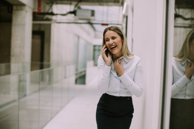 Ofis koridorunda cep telefonu kullanan genç ve güzel bir iş kadını.