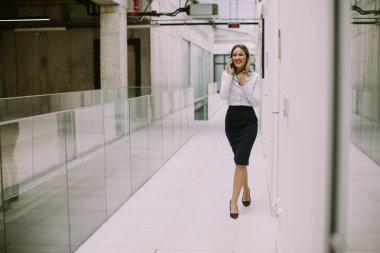 Ofis koridorunda cep telefonu kullanan genç ve güzel bir iş kadını.