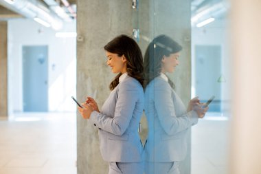 Ofis koridorunda cep telefonu kullanan genç ve güzel bir iş kadını.