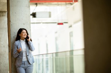 Ofis koridorunda cep telefonu kullanan genç ve güzel bir iş kadını.