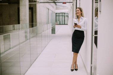 Ofis koridorunda cep telefonu kullanan genç ve güzel bir iş kadını.
