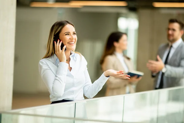 オフィスの廊下に携帯電話を持つ若いビジネス女性 — ストック写真