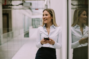 Ofis koridorunda cep telefonu kullanan genç ve güzel bir iş kadını.