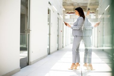 Ofis koridorunda cep telefonu kullanan genç ve güzel bir iş kadını.