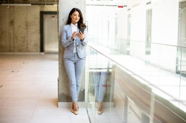 Ofis koridorunda cep telefonu kullanan genç ve güzel bir iş kadını.