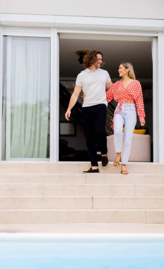 Evin arka bahçesindeki yüzme havuzunda merdivenlerden inen yakışıklı genç bir çift.