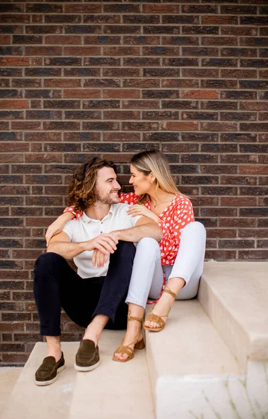 Tuğla Duvarın Önünde Oturan Güzel Gülümseyen Aşık Genç Bir Çift — Stok fotoğraf