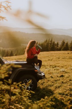 Pretty young woman relaxing on a terrain vehicle hood at countryside
