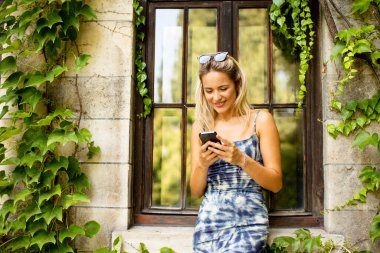 Sarmaşıklı eski evin yanında cep telefonu kullanan güzel genç bir kadın.