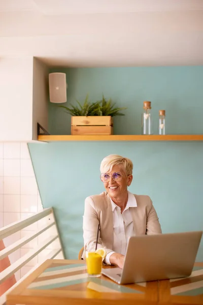 Senior Kvinna Som Använder Mobiltelefon Medan Arbetar Laptop Och Dricka — Stockfoto