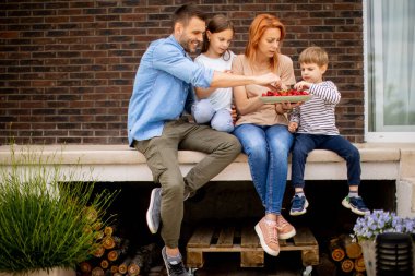 Family with a mother, father, son and daughter sitting outside on a steps of a front porch of a brick house and eating strawberries