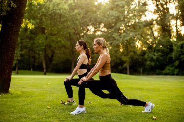 Parkta esneme hareketleri yapan iki sevimli genç bayan.