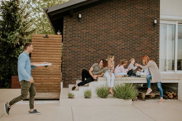 家の裏庭でピザを食べる準備をしている若者や子供たちの幸せなグループ — ストック写真
