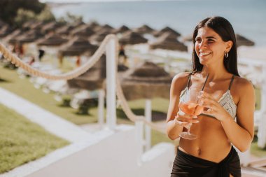 Gülümseyen genç kadın Bikini 'de kokteyl içerken tatilin tadını çıkarıyor.